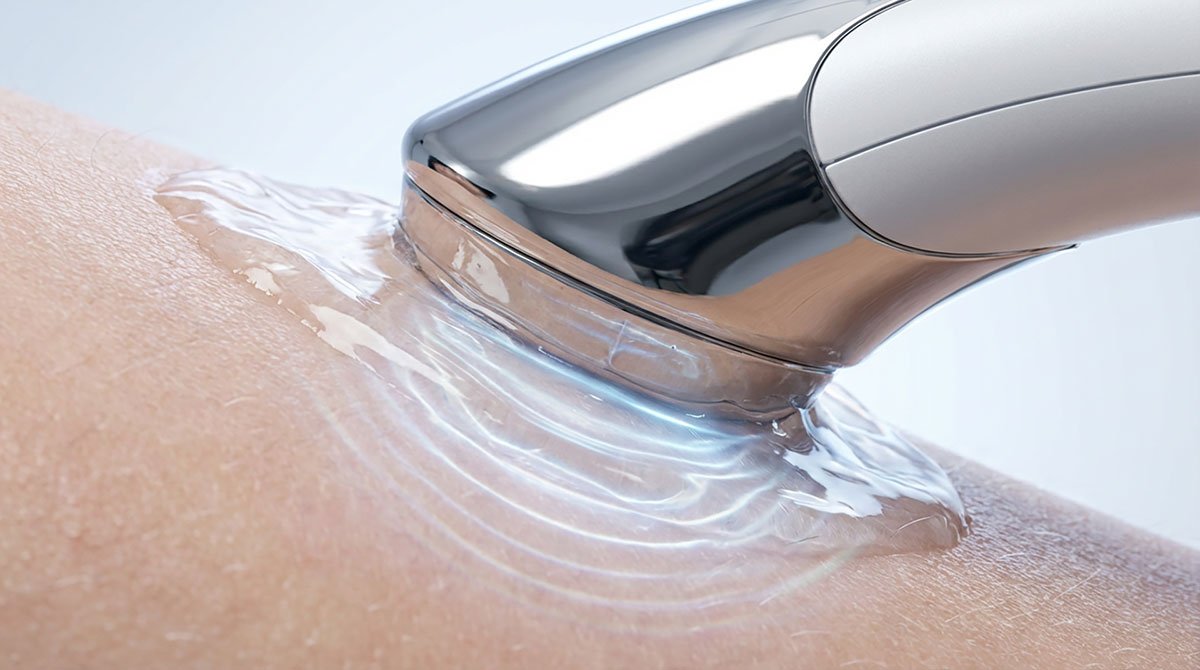 Macro close-up of an ultrasound skin treatment device applied on human skin with gel, showing rippling waves effect